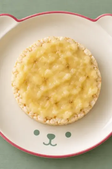 Reiswaffel mit Banane auf cremefarbenem Keramikgeschirr mit himbeerfarbenem Rand auf salbeifarbenem Holz.