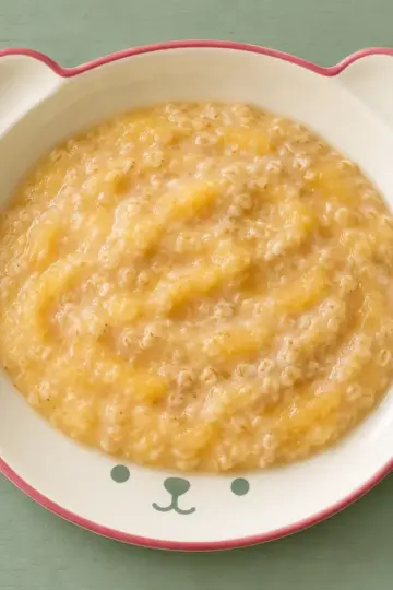 Dinkelporridge mit Pfirsichpüree auf cremefarbenem Keramikgeschirr mit himbeerfarbenem Rand auf salbeifarbenem Holz.